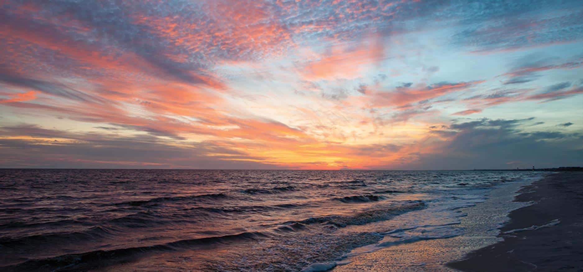 A breathtaking sunset over the ocean, with vibrant oranges and pinks spreading across the sky and reflecting on the water's surface.
