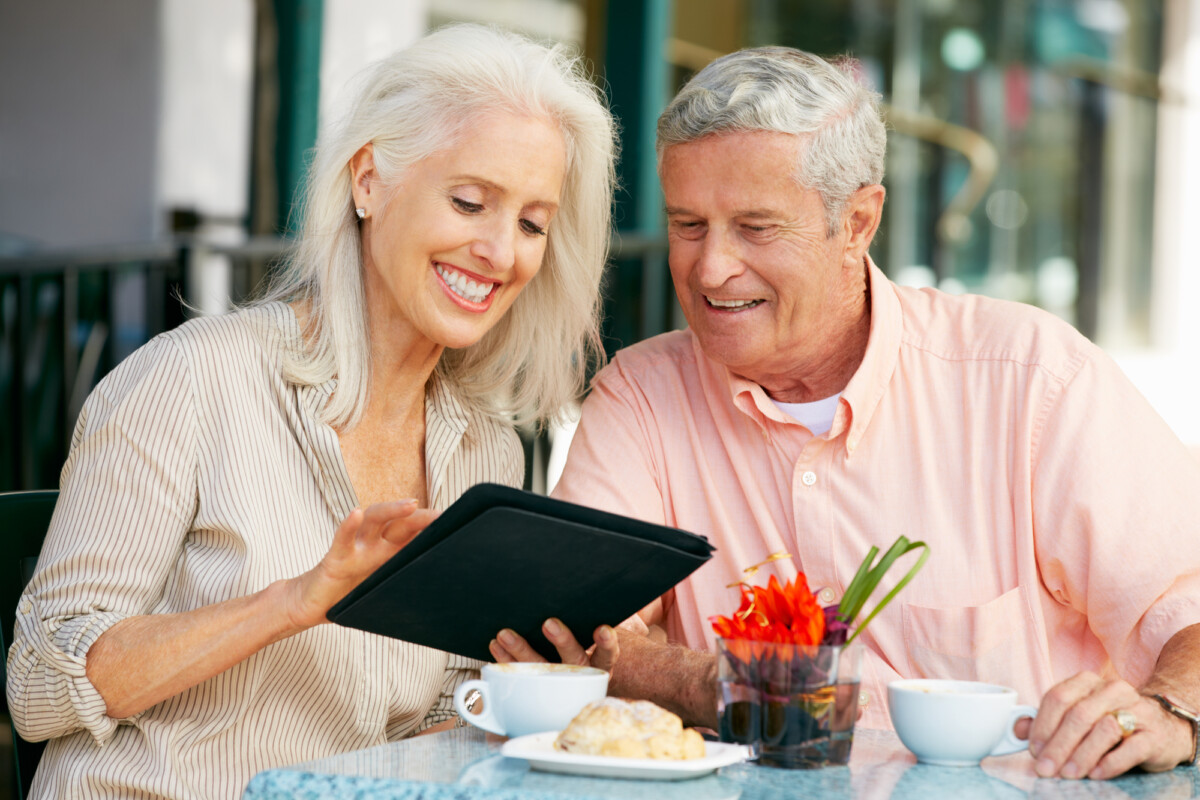 Senior couple enjoying a moment together at a cafe while looking at a tablet screen.